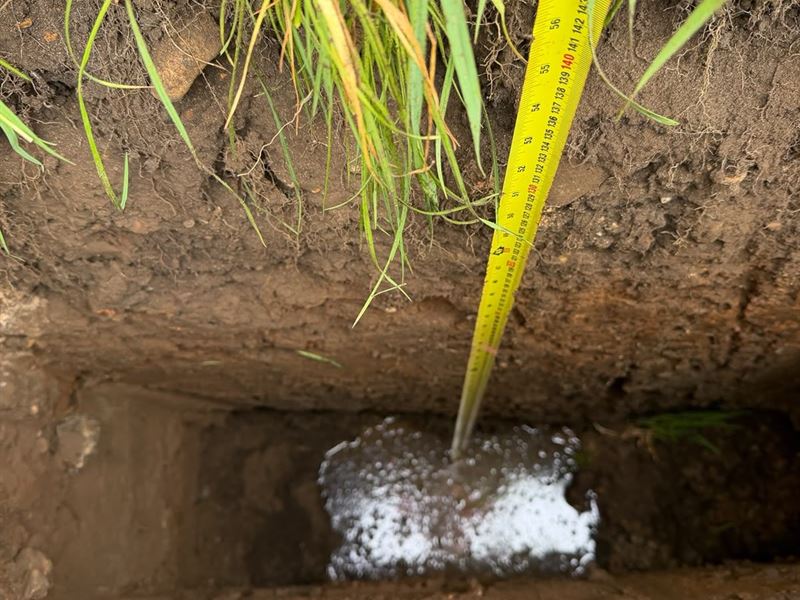 Water draining into the ground during a percolation test, with a tape measure recording the level