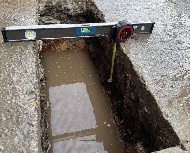 Trial pit with spirit level and tape measure recording depth
